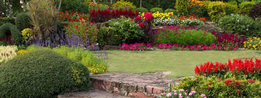 A landscaped garden with stone steps, manicured shrubs, and flower beds in full bloom